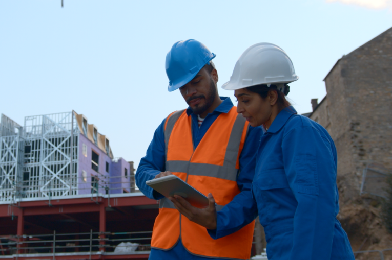 Two people on a construction site looking at a tablet device